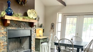 A dining area with a fireplace, a table with chairs, and a view of the outdoors.