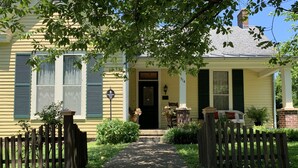 A yellow house with a front porch, a wooden fence, and a pathway leading to the entrance.
