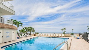 A swimming pool with lounge chairs and palm trees, a pool rules sign, and a view of the ocean.
