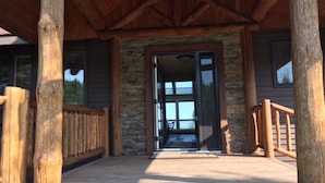 A wooden porch with a stone wall and a glass door leading to a covered entrance. - Unparalleled 180-degree Views of Lake Superior, 400 feet above the water! (Two Harbors)