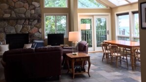 A spacious living area with a stone fireplace, comfortable seating, a television, and a large dining table. - Unparalleled 180-degree Views of Lake Superior, 400 feet above the water! (Two Harbors)