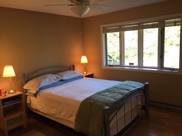 A bedroom with a bed, two bedside lamps, a window, and a ceiling fan.