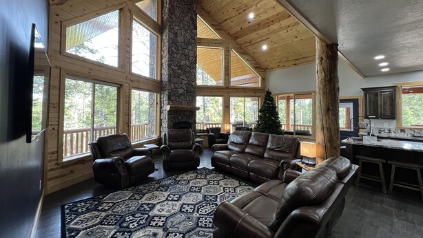 A spacious living area with a stone fireplace, leather sofas, and a large rug. - Large Cabin for Family & Friends to Enjoy - Close to many outdoor activities (Duck Creek Village)