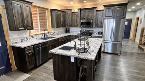 A modern kitchen with dark wood cabinets, stainless steel appliances, and a granite countertop. - Large Cabin for Family & Friends to Enjoy - Close to many outdoor activities (Duck Creek Village)
