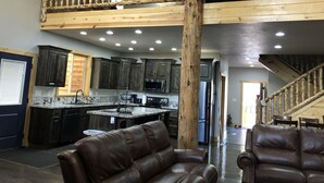 A spacious kitchen with dark wooden cabinets, a central island, and stainless steel appliances. There is a leather sofa and a staircase leading to an upper level. - Large Cabin for Family & Friends to Enjoy - Close to many outdoor activities (Duck Creek Village)