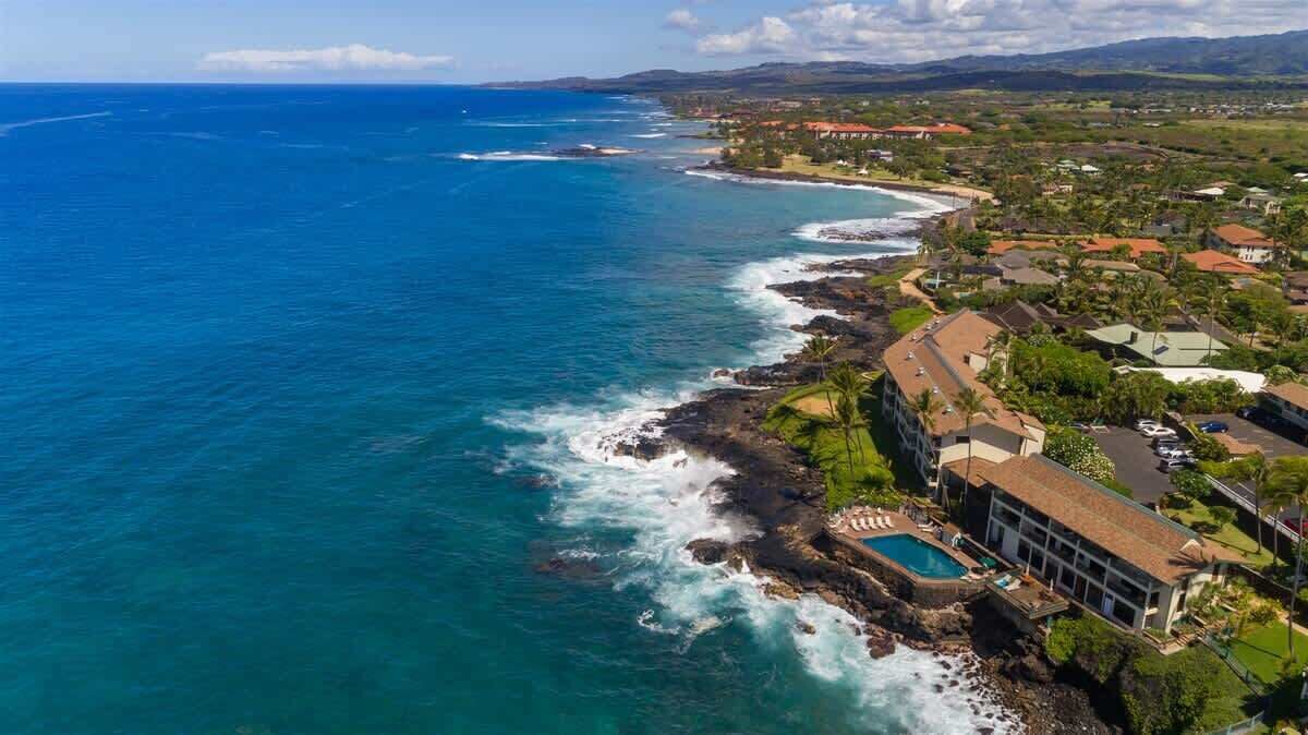 An aerial view of a coastal property with a swimming pool, ocean views, and a mix of residential and commercial buildings.