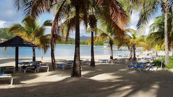 A beach with lounge chairs, palm trees, and a gazebo.