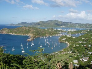A coastal area with numerous sailboats docked in a marina, surrounded by lush greenery and hills.