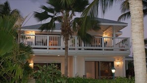 Una casa de dos pisos con un balcón, rodeada de vegetación tropical.