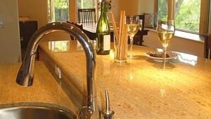 A kitchen with a granite countertop, stainless steel sink, and a hanging light fixture.