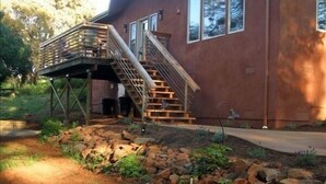 A modern house with a wooden deck and a staircase leading to a second floor.