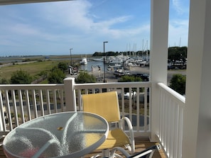 A balcony with a glass table and chairs, overlooking a marina with boats and a grassy area.