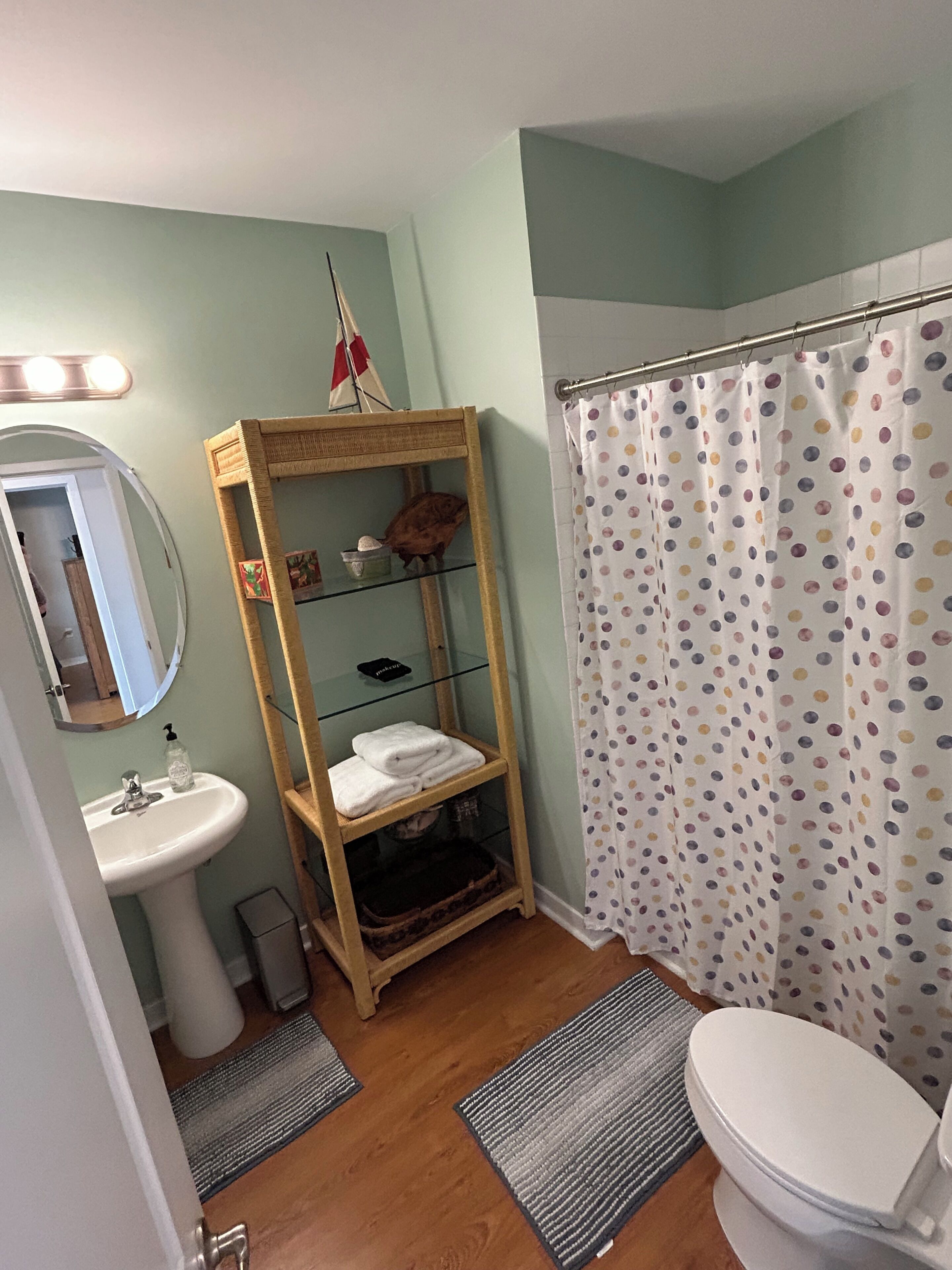 A bathroom with a wooden shelf, a sink, a toilet, and a shower curtain with a polka dot pattern.