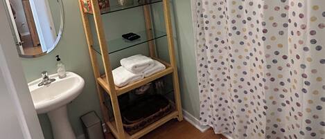 A bathroom with a wooden shelf, a sink, a toilet, and a shower curtain with a polka dot pattern.