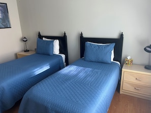 Two twin beds with matching blue bedding, a bedside table with a lamp, and a small decorative box on the nightstand.