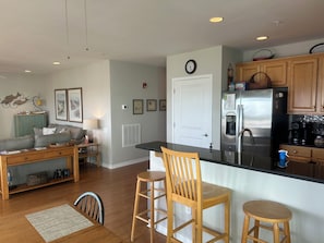 A modern kitchen with a central island, wooden bar stools, a dining table with chairs, a sofa, and a decorative wall piece.