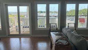 En stue med sofa, et træbord og udsigt til en lystbådehavn gennem store vinduer.