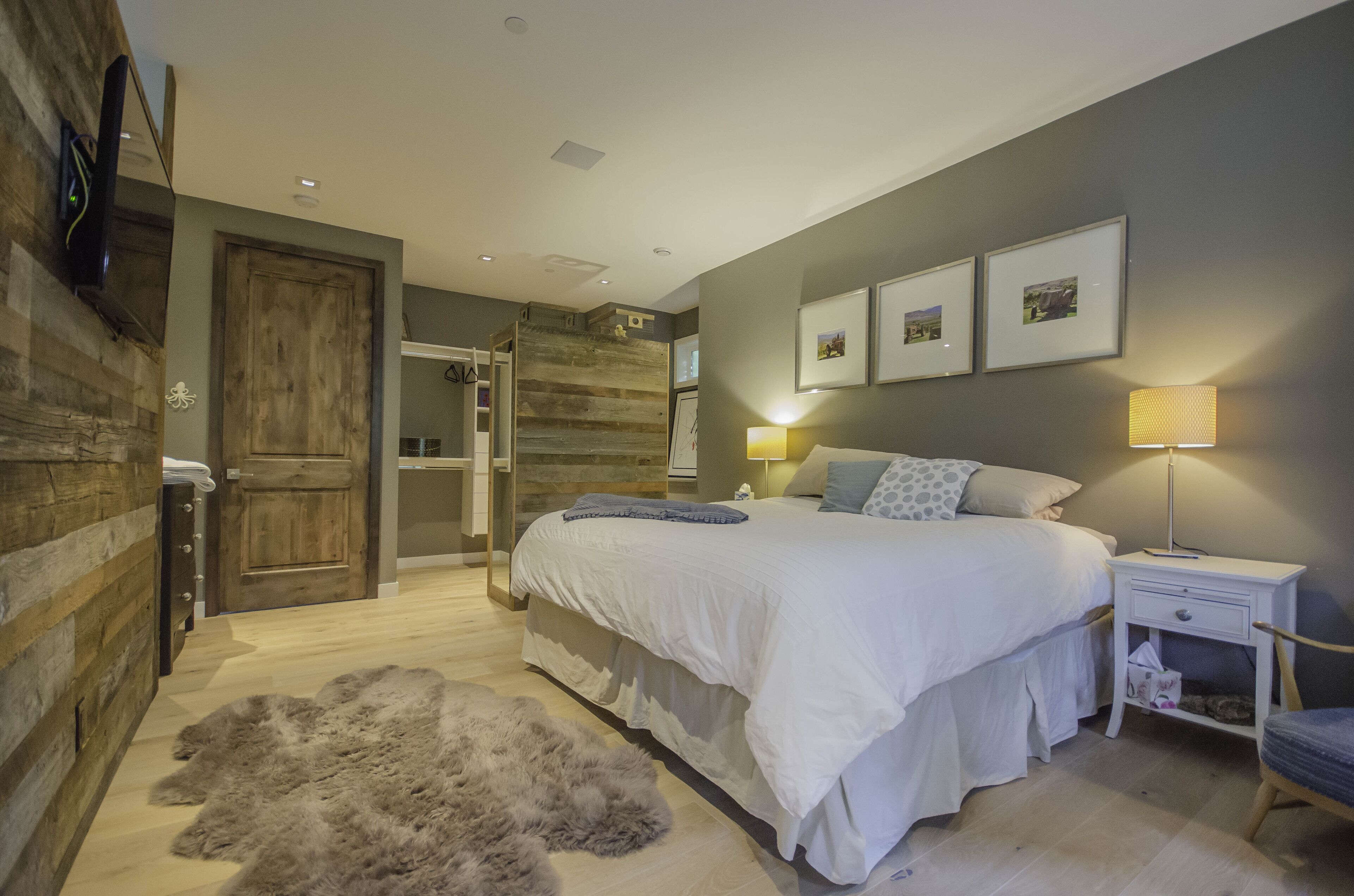 Une chambre avec un grand lit, une porte en bois, un tapis moelleux et une table de chevet avec une lampe.