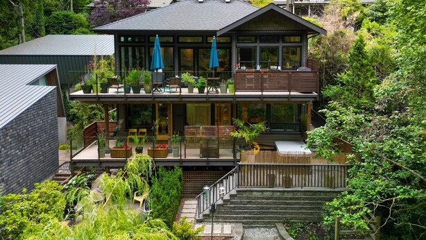 A modern two-story house with a balcony, outdoor seating, and a view of the surrounding greenery. - West Coast Designer Home - Ocean & Forest (District of North Vancouver)