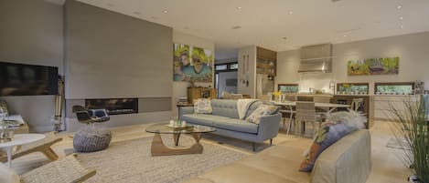 A modern living room with a sofa, coffee table, and seating area. There is a kitchen area with a dining table and chairs.