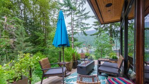 A deck with outdoor furniture, a blue umbrella, and a view of a forested area. - West Coast Designer Home - Ocean & Forest (District of North Vancouver)