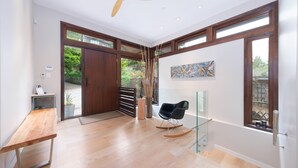 A spacious room with a wooden floor, a rocking chair, a glass table, and a large window with a view of greenery. - West Coast Designer Home - Ocean & Forest (District of North Vancouver)