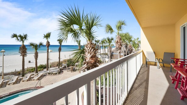 Ein Balkon mit Blick auf einen Strand, Palmen und einen Pool.