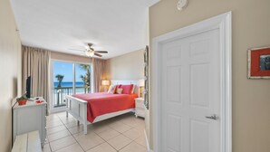 Ein Hotelzimmer mit Bett, Schreibtisch, Stuhl, Deckenventilator, Tür und Blick auf den Strand.