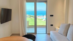 Un saló modern amb un sofà, una taula de dinar amb cadires, un televisor penjat a la paret i una porta corredissa de vidre que dona a un balcó amb vistes al mar.