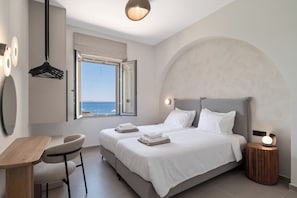 A bedroom with a bed, bedside table, chair, and a view of the sea through an open window.