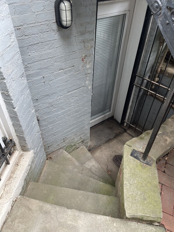 A concrete staircase leading to a door with a metal gate, a wall with a textured surface, and a metal object on the wall.