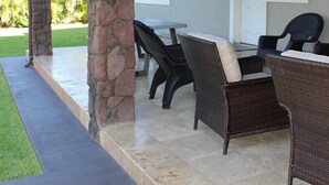 Une terrasse extérieure avec des piliers en pierre, des meubles en osier et un espace abrité doté d’un ventilateur de plafond.
