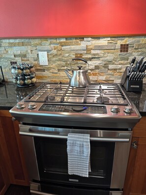 A kitchen with a gas stove, oven, and a stone backsplash. - Lieutenant's Suite - Romantic Luxury 1 Bedroom Loft, Easy Access to Beach & Town (Eastsound)