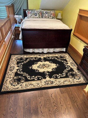 A bedroom with a large bed, a wooden headboard, a bedside table with a lamp, and a decorative rug. - Lieutenant's Suite - Romantic Luxury 1 Bedroom Loft, Easy Access to Beach & Town (Eastsound)