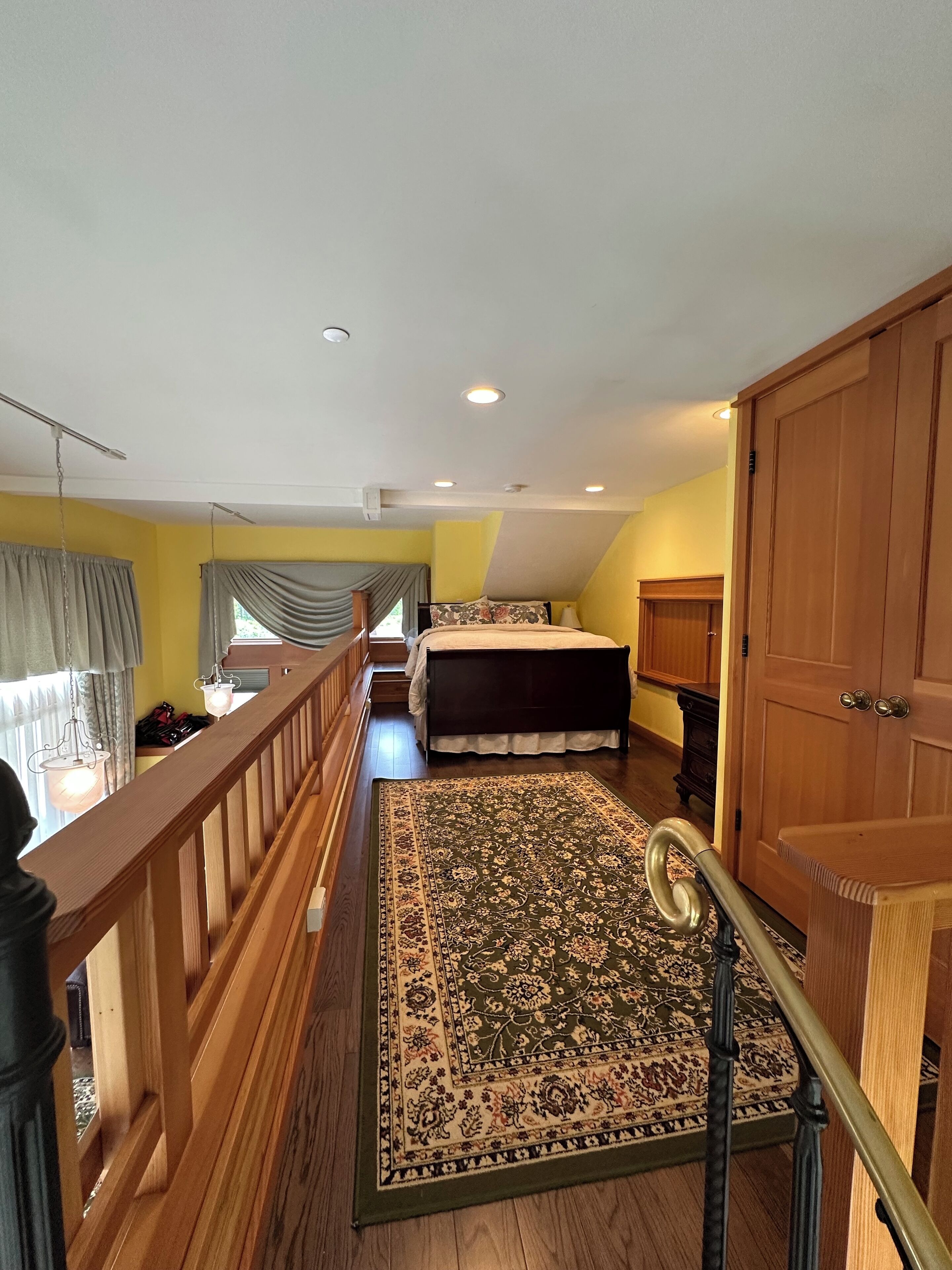 A bedroom with a large bed, a wooden floor, a balcony with a railing, and a view of the outside.