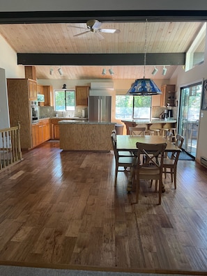 A spacious kitchen with wooden cabinets, a central island, and a dining area with a table and chairs. - Cozy, family-friendly cabin in a gated lake resort near Yosemite!  (Groveland)
