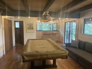 A room with a large table, a sofa, and a window with a view of trees. - Cozy, family-friendly cabin in a gated lake resort near Yosemite!  (Groveland)