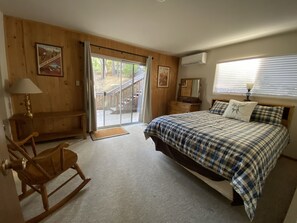 Um quarto com uma cama grande, uma poltrona de balanço, um aparador de madeira e uma porta de correr para uma área externa.
