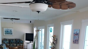 Amplia sala de estar con una mesa de comedor de vidrio rodeada de sillas de mimbre, un ventilador de techo y un televisor de pantalla plana grande.