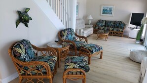 Un salón con muebles de mimbre, un sofá blanco y un televisor.