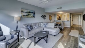 A modern living room with a grey sofa, a coffee table, and a dining area with a kitchen in the background. - 404 Captain's Walk: Perfect 2BR/2Bth Oceanfront Condo (Hilton Head Island)