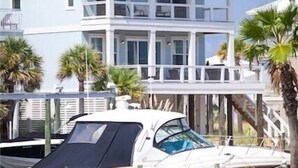 A two-story house with a balcony, a boat docked in front, and palm trees. - Waterfront Home with Golf Cart, Kayaks, Bikes and Paddleboards! (Navarre Beach)