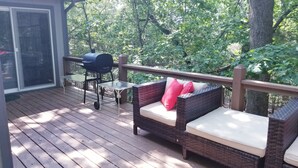 Eine überdachte Terrasse mit Korbmöbeln, einem Grill und einem Glastisch.