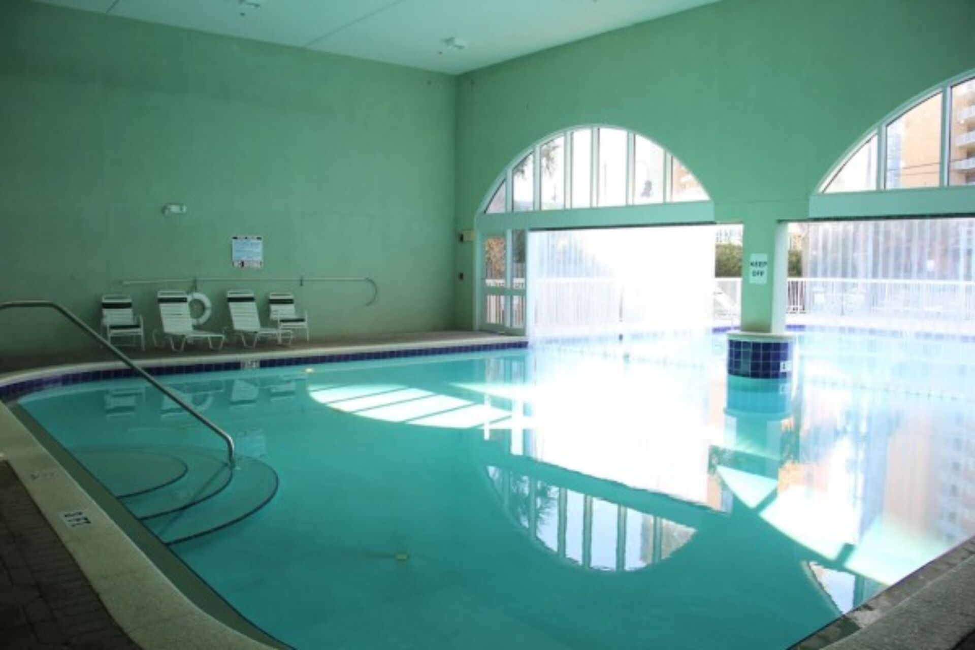 An indoor swimming pool with clear water, a tiled floor, and a few lounge chairs.