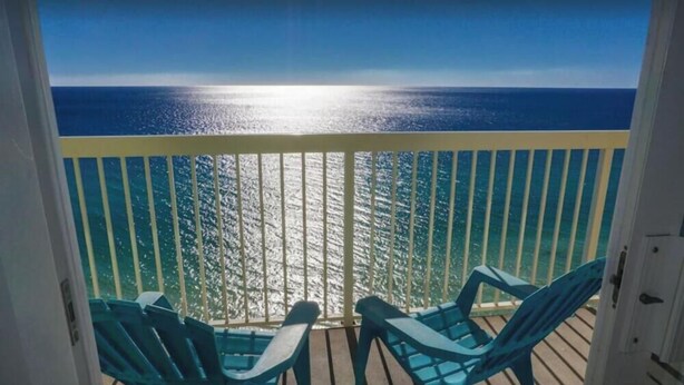 En balkon med to turkise stole, der vender ud mod udsigten over havet.