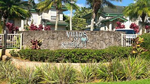 Villas of Kamala with a stone wall entrance, palm trees, and a clear blue sky. - Walk to Beach & Sunset-Luxury - Golf Course -2000sq ft - 3BR Pool&Jacuzzi (Princeville)