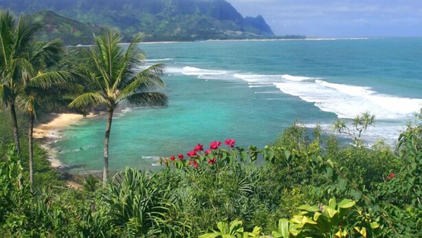 A tropical beach with clear turquoise waters, palm trees, and a mountainous backdrop. - Walk to Beach & Sunset-Luxury - Golf Course -2000sq ft - 3BR Pool&Jacuzzi (Princeville)