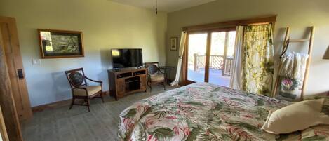 Ein Schlafzimmer mit einem Bett, einem Fernseher, einem Schreibtisch und einem Balkon.