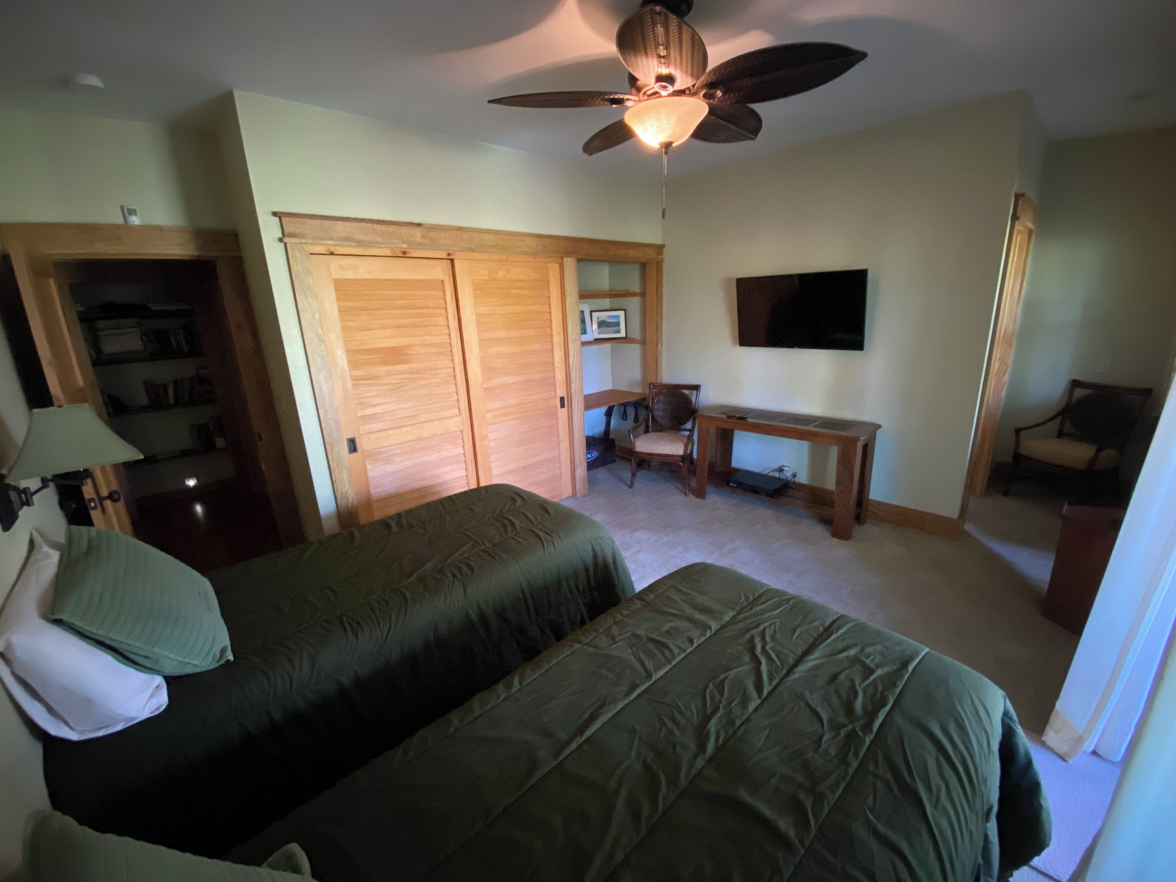 Une chambre avec deux lits, un bureau, une chaise, un ventilateur de plafond et un téléviseur.