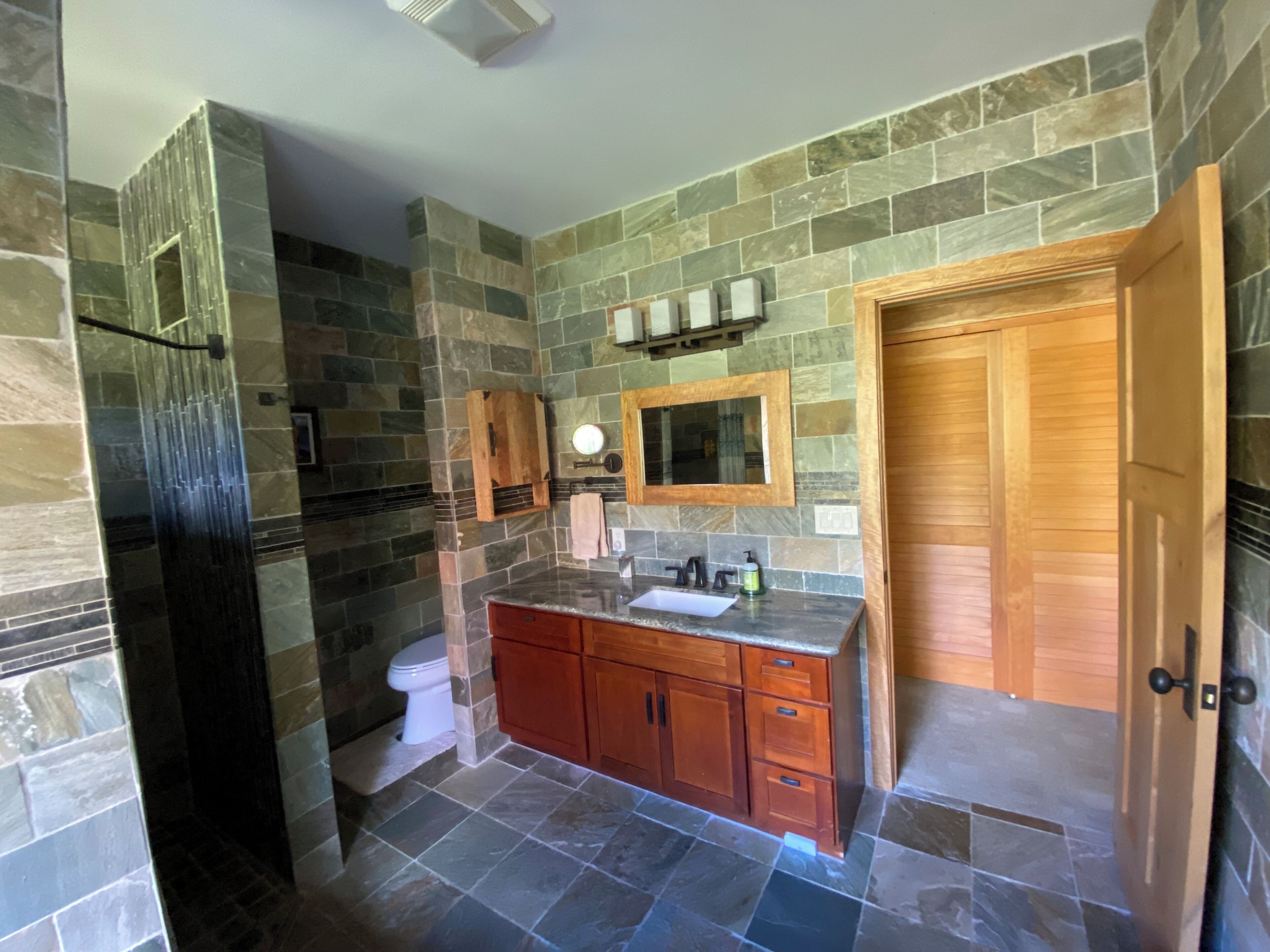 A bathroom with stone walls, a wooden vanity, a toilet, and a mirror.